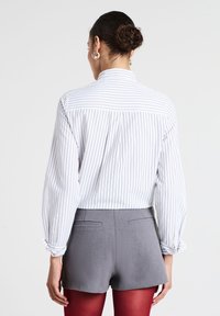 Camicia a righe bianche e grigie con yoke dietro, maniche arrotolate e colletto, abbinata a pantaloni grigi e collant rossi.