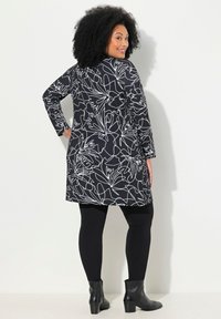 Tunique noire à motifs floraux avec des manches longues, dotée de contours blancs. Portée sur des leggings noirs et assortie à des bottes noires à la cheville.