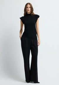 Zwart mouwloos top met gerimpelde schouderaccenten gecombineerd met zwarte wijde broekspijpen. Gladde textuur van de stof en nauwsluitend ontwerp.