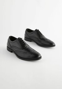 Musta nahkakengät Oxford-tyyliin, joissa on brogue- yksityiskohtia, pyöreä kärki ja nauhakiinnitys, matalalla korolla.
