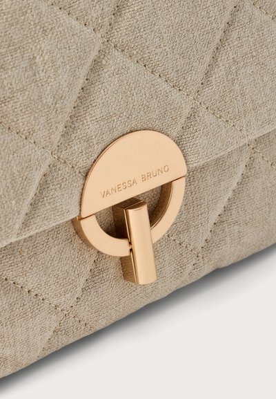 Gros plan sur un sac à main tissé beige avec un fermoir doré gravé « Vanessa Bruno ».