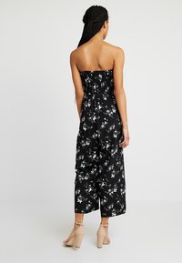 Mono negro de flores con diseño sin tirantes, corsé fruncido, pantalones de pierna ancha y patrones de flores coloridas sobre un fondo oscuro.