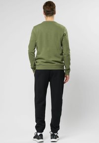 Olijfgroene sweatshirt met een ronde halslijn en ribbels aan de manchetten, gecombineerd met zwarte joggers met elastische zoom en zwarte sportschoenen.
