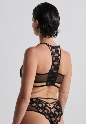 Ensemble de lingerie en mesh noir avec des détails en boucle complexes. Le soutien-gorge a un design dos nageur, et la culotte dispose de sangles ajustables avec un accent doré.
