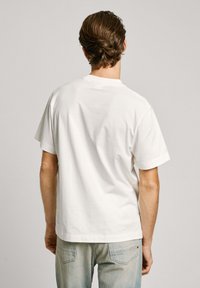 Balta kokvilnas T-kreklu ar brīvu piegriezumu, apaļu kakla līnijai, īsām piedurknēm un vienkāršu aizmuguri. Pievilcīga šuvju detaļa ap kakla izgriezumu.