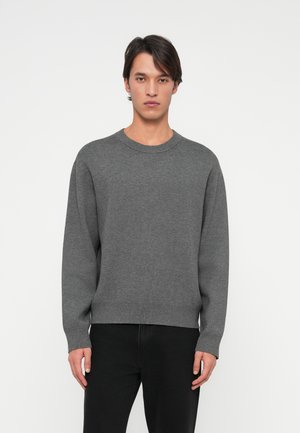 Gråstickad tröja med rundhals, långa ärmar och ribbad nederkant. Bärs över mörka jeans, har en slät textur och en avslappnad passform.