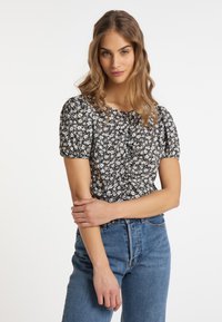 Sort blomsterbluse med puffærmer, tekstureret stof, hvide tusindfryd og rund halsudskæring, parret med højtaljede blå jeans.