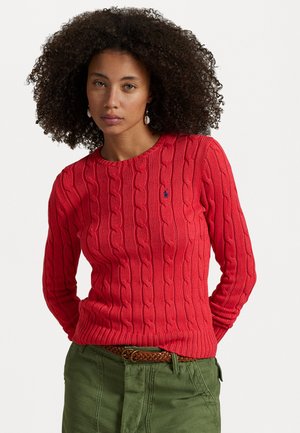 Suéter rojo de punto con un patrón de trenzas, cuello redondo y mangas largas. Se lleva con pantalones verde oliva y un cinturón trenzado marrón.
