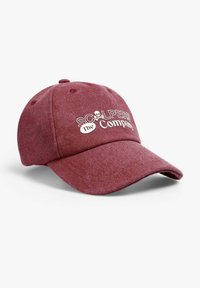 Gorra de béisbol color burdeos hecha de tela texturizada. Presenta un logo bordado en blanco con un diseño de calavera. Visera curva y correa ajustable en la parte trasera.
