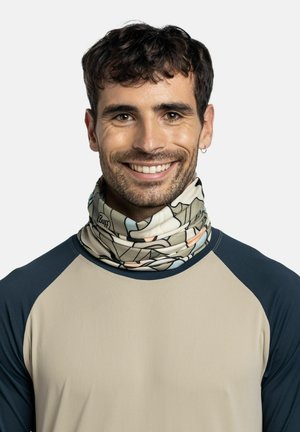 Uomo sorridente con capelli corti e scuri che indossa una camicia beige e blu navy e una sciarpa multicolore con motivo e logo "Buff".