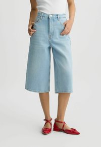 Jeans culotte decolorate, cu talie înaltă, cu un fit lejer și tiv brut, asortați cu pantofi joși din piele roșie, cu un accent în formă de fundiță.