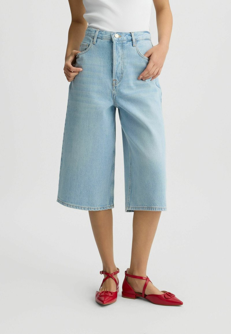 Jeans culotte decolorate, cu talie înaltă, cu un fit lejer și tiv brut, asortați cu pantofi joși din piele roșie, cu un accent în formă de fundiță.