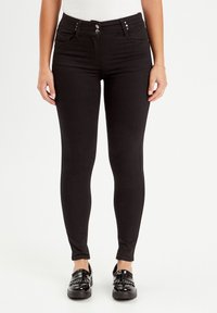 Sorte stretch jeans med høj talje, fem lommer og knapdetaljer. Slim fit design med en glat tekstur. Sættet kompletteres med skinnende sorte sko.