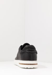Sneaker in pelle nera con forma arrotondata, suola in gomma bianca texturizzata e una rifinitura in sughero lungo il tallone. Design liscio e minimalista.