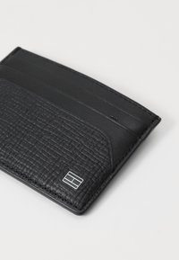 Black leather cardholder with a textured surface, featuring smooth sections, multiple card slots, and a small metallic logo detail.