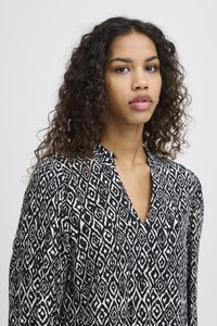 Camicia a maniche lunghe in bianco e nero con motivo a righe, dal taglio morbido, colletto e design geometrico a rombi.