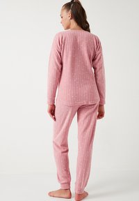Roze pidžama koja sadrži rebrastu teksturu, duge rukave i male bijele točke na majici i hlačama. Udoban kroj s elastičnim manžetama.
