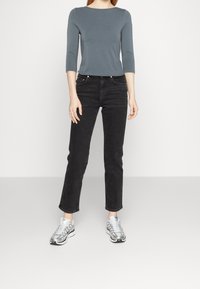 Grått åtsittande topp med trekvartsärmar, i kombination med högmidjade svarta jeans och silverfärgade sportskor. Enkelt, modernt design.