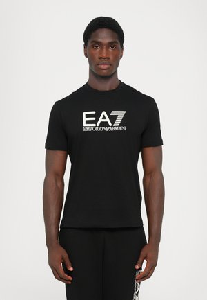 T-shirt noir en coton doux, avec un logo EA7 Emporio Armani blanc bien visible sur le devant. Design à manches courtes et col rond.