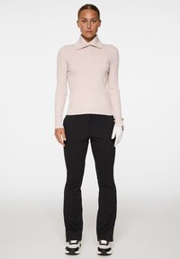 Jasnoróżowa koszula polo z długim rękawem, z kołnierzykiem i zapinana na guziki, w połączeniu z czarnymi spodniami o slim fit oraz białą rękawicą golfową.