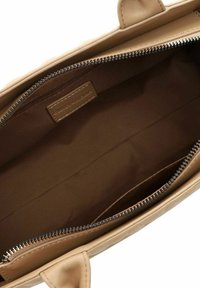 Intérieur d'un sac à main en cuir beige, caractérisé par une texture lisse, une poche zippée et un compartiment principal spacieux avec une doublure marron.