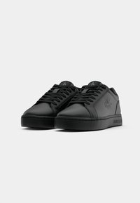 Zwarte lage Calvin Klein sneakers met veters, reliëflogo aan de zijkant en gemerkte zool, gepresenteerd op een witte achtergrond.