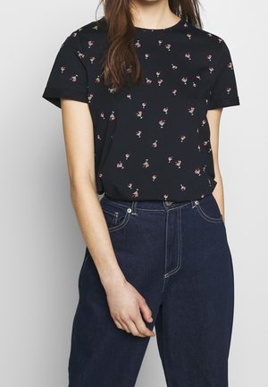 T-shirt noir avec un petit motif floral en rose et blanc, manches courtes, col rond, associé à un jean bleu foncé taille haute.