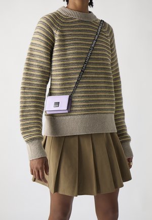 Persona que lleva un suéter de manga larga a rayas, falda plisada caqui y una pequeña bolsa cruzada lavanda con una correa negra de marca.