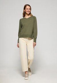 Olivgrön stickad tröja med v-ringning och långa ärmar, tillsammans med ljusbeige raka byxor och ljusa sneakers.