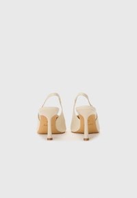 Scarpe con tacco alto beige con design slingback, punta affilata, texture in pelle liscia e tacco sottile. Branding visibile sulla soletta.