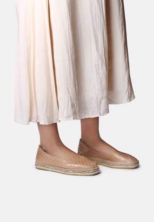 Plochá obuv v telovej farbe s perforovanými detailmi a zlatým akcentom pri podrážke. Nosí sa s ľahkou, prúdiacou sukňou v krémovej farbe.