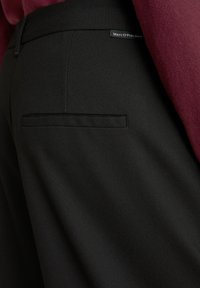 Zwarte op maat gemaakte broek van gestructureerde stof, met een enkele achterzak en een klein merklabel op de tailleband.