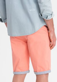 Shorts corallo con orlo risvoltato, realizzati in tessuto leggero. Abbinati a una camicia di jeans azzurro chiaro. Design semplice e casual.