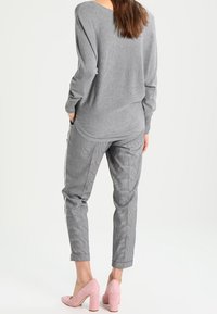 Grå strikket bluse med lange ærmer parret med grå mønstrede bukser, der har en slim fit og lyserøde højhælede sko. Enkel, struktureret design.