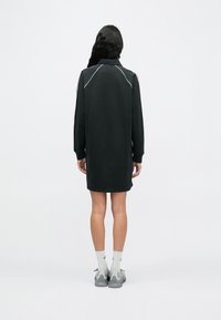 Μαύρο φόρεμα φούτερ με μακριά μανίκια, ψηλό λαιμό και λευκές ραφές ως διακοσμητικά στοιχεία. Φορεμένο με γκρι αθλητικά παπούτσια και κάλτσες με ανοιχτό σχέδιο.