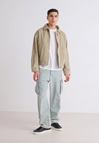 Chaqueta beige de canalé, camiseta blanca, pantalones cargo azul claro, zapatillas negras. Corte slim con botones a presión y bolsillos laterales.