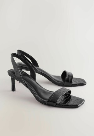 Fekete sarokszandál krokodilbőr hatású anyagból, nyitott orral és hátsó pántos kialakítással. Négyzet alakú orra és karcsú, közepes magasságú sarka van.