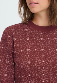 Sudadera burdeos con un patrón texturizado de círculos interconectados y motivos florales en rosa claro. Cuello acanalado.