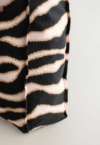 Sort og beige tigerstribet mønstret stoffolder, der danner en del af et blødt rektangulært objekt, mod en hvid baggrund.