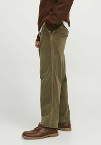 Green corduroy pants with a straight cut and side pockets, paired with brown leather shoes featuring a rubber sole.