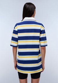 Polo à manches courtes bleu et jaune à rayures avec un col blanc, présentant une coupe décontractée et un tissu doux et texturé.