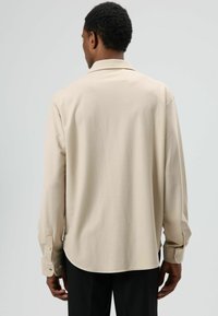 Beige overhemd met lange mouwen, een omgeslagen kraag en met knopen sluitbare manchetten, gemaakt van gladde stof. Heeft een afgeronde zoom en een losse pasvorm.