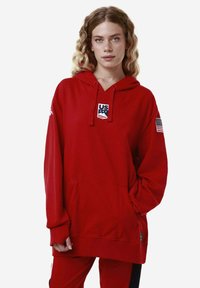 Felpa rossa con cappuccio, tasca frontale, patch con logo "US" e bandiera americana sulla manica. Realizzata in un morbido tessuto compatto.