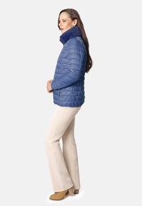 Chaqueta acolchada azul con cuello alto, combinada con pantalones de pajarita beige claro y botas de tacón color caramelo. Textura suave en toda la prenda.