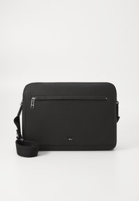 Sac messenger en cuir noir avec une texture, poche zippée avant, bandoulière ajustable et détail de logo en bas.