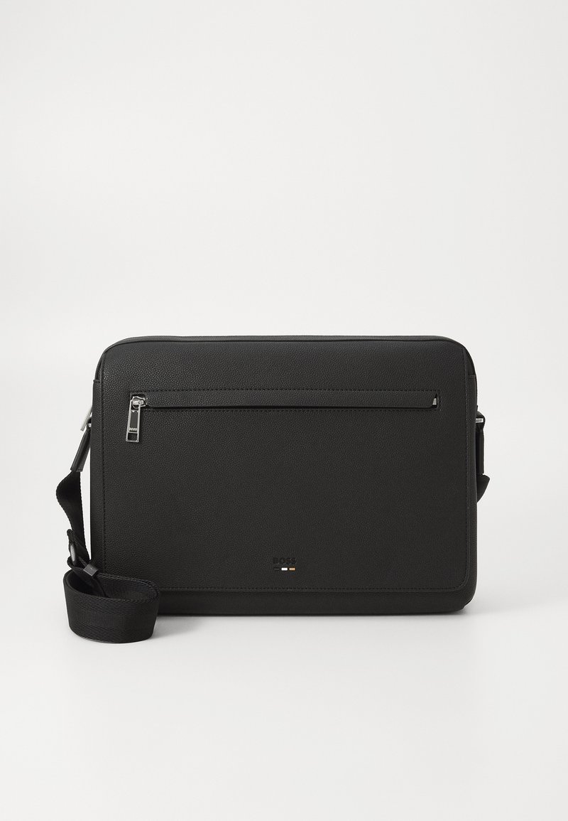 Sac messenger en cuir noir avec une texture, poche zippée avant, bandoulière ajustable et détail de logo en bas.