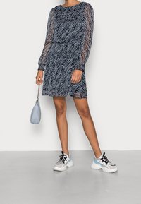 Mini-robe imprimé zèbre en tissu bleu marine transparent avec manches longues bouffantes et poignets élastiques, associée à un sac à main bleu clair et des baskets.