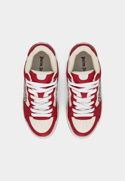 Ζευγάρι κόκκινων και άσπρων sneakers με κορδόνια και μαύρο λογότυπο στο πλάι, φωτογραφημένα από πάνω σε απλό λευκό φόντο.