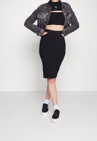 Schwarzer gerippter Strickrock und passendes Cropped-Top mit Ausschnittdetails, kombiniert mit einer Jeansjacke. Fußbekleidung: schwarze Schuhe mit weißen Sohlen.