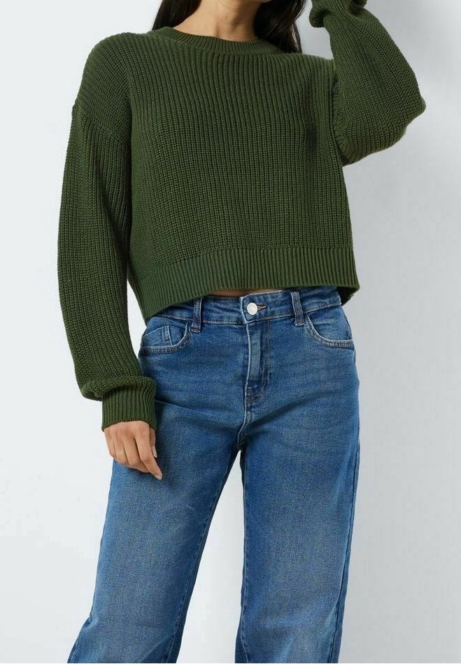 Green knitted sweater with a cropped design, ribbed texture, and long sleeves paired with light blue denim jeans.